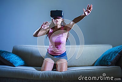 Young woman at home sofa couch playing video game using VR virtual reality goggles watching in 3 dimension enjoying curious having Stock Photo