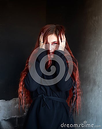 Young woman in horrible dark room on background of black wall, portrait of frightened and desperate girl Stock Photo