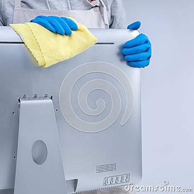 Young woman housekeeper in apron is doing cleaning silver computer screen with blue gloves, wet yellow rag, close up, copy space, Stock Photo