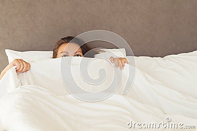 A young woman with huge frightened open eyes lying in bed and covers herself with the sheets and hides. Nightmares, insomnia, phob Stock Photo
