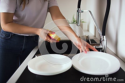Young woman in kitchen during quarantine. Cut view of girl`s hands holding sponge with dishwasher and take one white Stock Photo