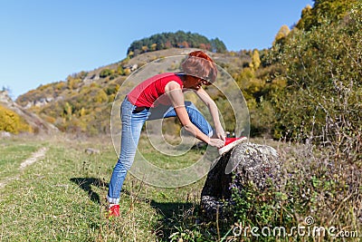 Young woman laces up the jogging shoes against the blue sky and forest after a pedestrian walk sunny day Stock Photo