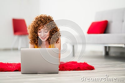Young woman laying on a red pluffy carpet and using her laptop. Stock Photo