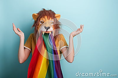 Young woman in lion mask with rainbow pride lgbt flag in mouth with raised hands and shrugging shoulders, confused expression Stock Photo