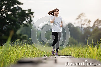 Woman listening music on earphones while running on wooden path in field Stock Photo
