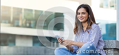 Young woman listening to music and looking at the camera outdoor with copy space Stock Photo