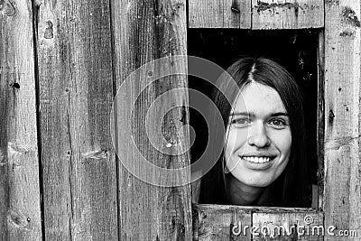 A young woman locked in a wooden shed, peeking through a small window. Stock Photo