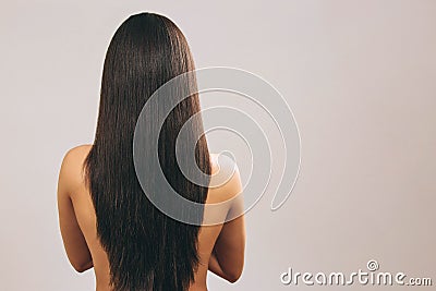 Young woman with long black hair posing on camera. Showing lenght of it. Smooth treasure. Standing back to camera. Naked Stock Photo