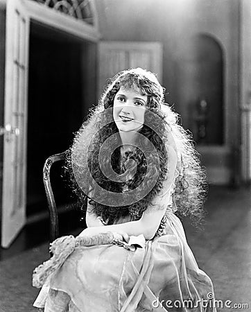 Young woman with long Curls, Curly Hair, Curly sitting on a chair and smiling Stock Photo