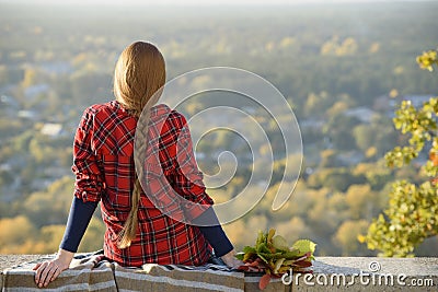 Young woman with long hair sits on a hill overlooking the city Stock Photo