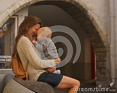 Young woman with long hair sitting on bench and hugging little baby. Baby and mother laughing. Family love and sincerity Stock Photo