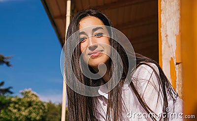 A young woman looks out from the balcony.The bright sun shines on the girl. Beautiful brunette girl enjoys the sun Stock Photo