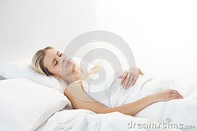 Young woman lying in the bed. Beautiful blond sleeping girl. Morning in the bedroom, daylight from the window. Health Stock Photo