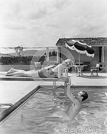 Young woman lying on a diving board with a young man hanging from it Stock Photo