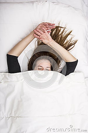Young woman is lying in her bed with closed eyes, smiling under her blanket after a restful sleep. Stock Photo
