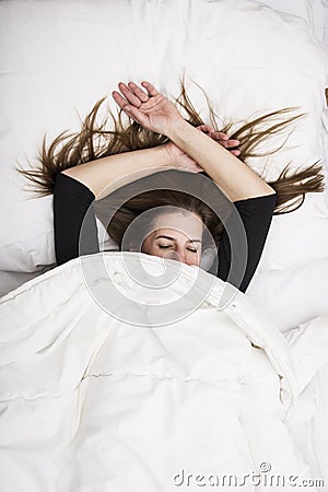Young woman is lying in her bed with closed eyes, smiling under her blanket after a restful sleep. Stock Photo