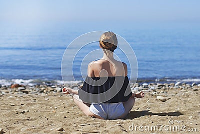 Young woman makes meditation in lotus pose on sea / ocean beach, harmony and contemplation. Beautiful girl practicing yoga at sea Stock Photo