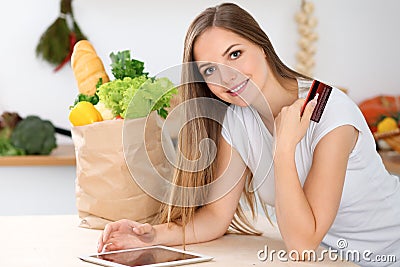 Young woman is making online shopping by tablet computer and credit card. Housewife found new recipe for cooking in a Stock Photo