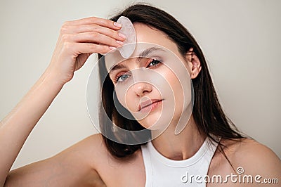 Young woman massages forehead with a quartz gua sha scraper Stock Photo