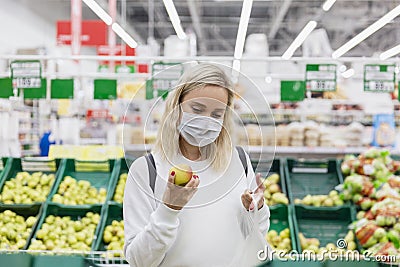 Young woman in a medical mask chooses apples in a supermarket. Healthy eating. Coronavirus pandemic Stock Photo