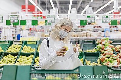 Young woman in a medical mask chooses apples in a supermarket. Healthy eating. Coronavirus pandemic Stock Photo