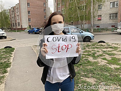 Young woman in medical mask holding sheet with inscription covid19 stop. Adult female protecting yourself from diseases Stock Photo