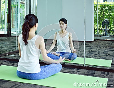 Young woman meditating in front of mirror in yoga room, Yoga con Stock Photo