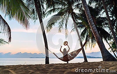 Young woman meeting sunrise sitting in hammock on the sand beach under the palm trees Stock Photo