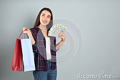 Young woman with money and shopping bags on light grey background. Space for text Stock Photo