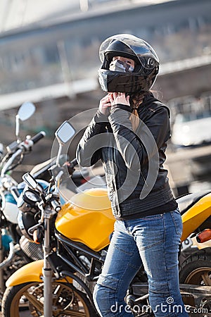 Young woman motorcyclist buttons black crash helmet for riding bike on urban road Stock Photo