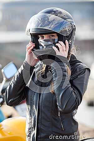 Young woman motorcyclist put on crash helmet for riding bike on urban road Stock Photo