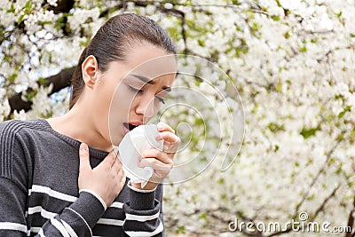 Young woman with nose wiper near blooming tree. Allergy concept Stock Photo