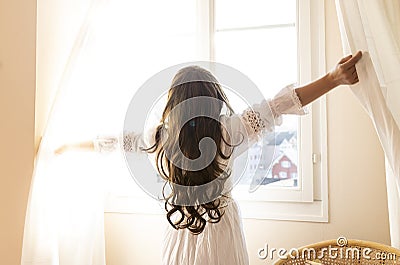 Young woman open a curtains and stretching in bed after waking up Stock Photo