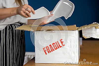 Young woman opening damaged delivery package,online shopping package. Broken fragile plate at home Stock Photo