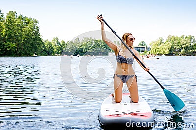 Young woman paddling on sup board on a lake. Active woman on modern trendy stand up paddle board. Summer outdoors Stock Photo