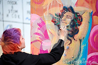 Young woman painter painting multicolored picture on large canvas, outdoor art performance festival Editorial Stock Photo