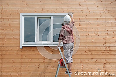 A young woman paints the outside wall of a new wooden house Stock Photo