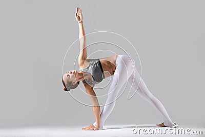 Young woman in Parivrrta Trikonasana pose, grey studio backgroun Stock Photo