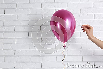 Young woman piercing bright balloon near wall, space for text Stock Photo