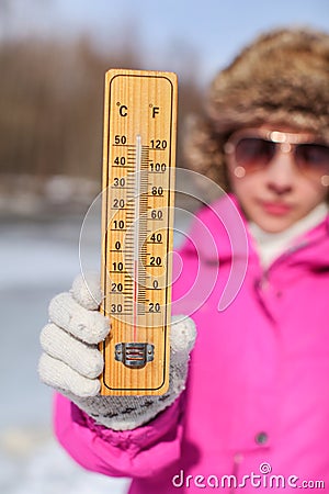 Young woman in pink winter jacked, gloves and furry hat holding thermometer that is showing -5 degrees. Winter / cold days coming Stock Photo