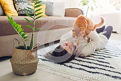 Young woman playing with cat on carpet at home. Master lying on floor with her pet Stock Photo