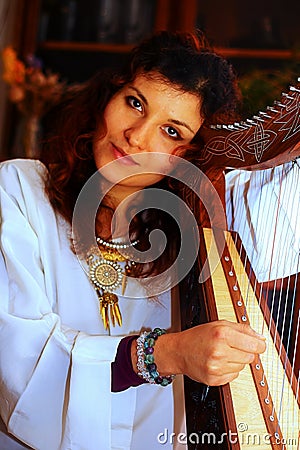 Young woman playing celtic harp in a white angelic historical costume. Stock Photo
