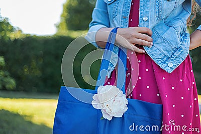 Young woman in polka dot dress and denim jacket with bag with peony in the park, image without face, fashion outfit concept Stock Photo