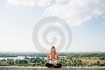 Young woman practices yoga outside. Girl calm and peaceful sits on parapet in lotus position. Her fingers fold into sign Stock Photo