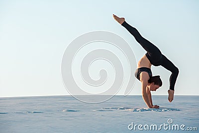 Young woman practicing inversion balancing yoga pose handstand on sand. Stock Photo