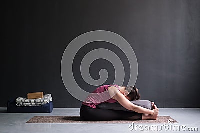 Woman practicing yoga, doing Seated forward bend pose, using bolster. Stock Photo