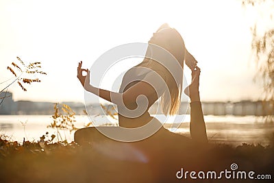 Young woman practicing yoga exercise at river beach and city background Stock Photo