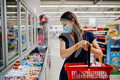 Young woman with protective face mask shopping for groceries in indoor groceries store.Coronavirus COVID-19 concept.Mandatory face Stock Photo