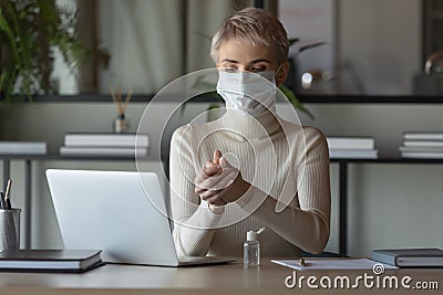 Female employee cleanse hands with sanitizer at workplace Stock Photo