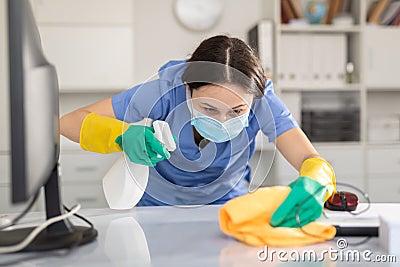Young woman in a protective mask, cleaning the office, wipes the desktop Stock Photo